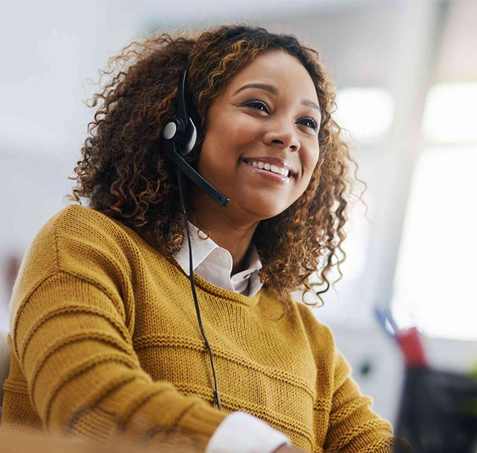 An IT Helpdesk Administrator sits at a desk with dual screens, providing remote assistance and troubleshooting to users, with a headset on and system dashboards visible on one monitor.